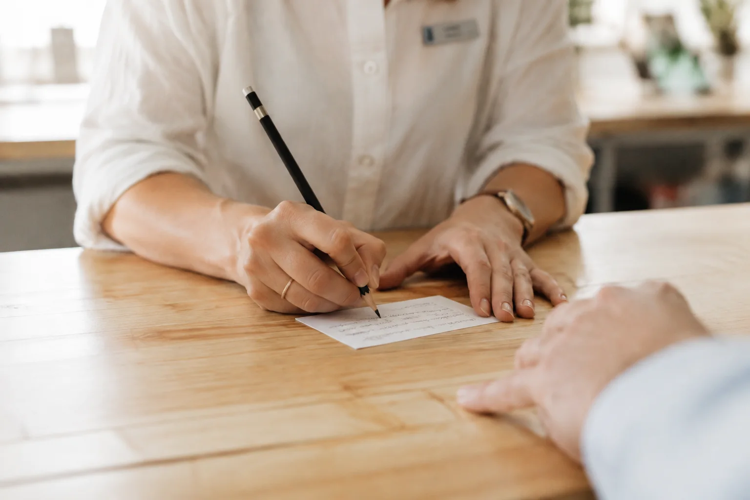 A person writing a short detail on a card for someone across a table