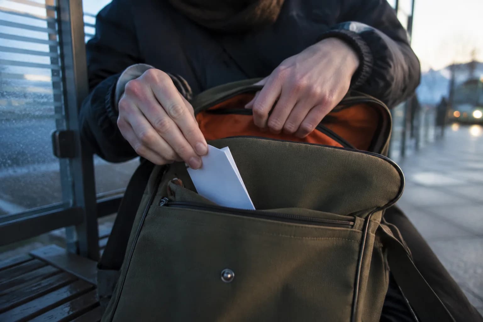 A learner placing a small review card into a bag beside a bus stop