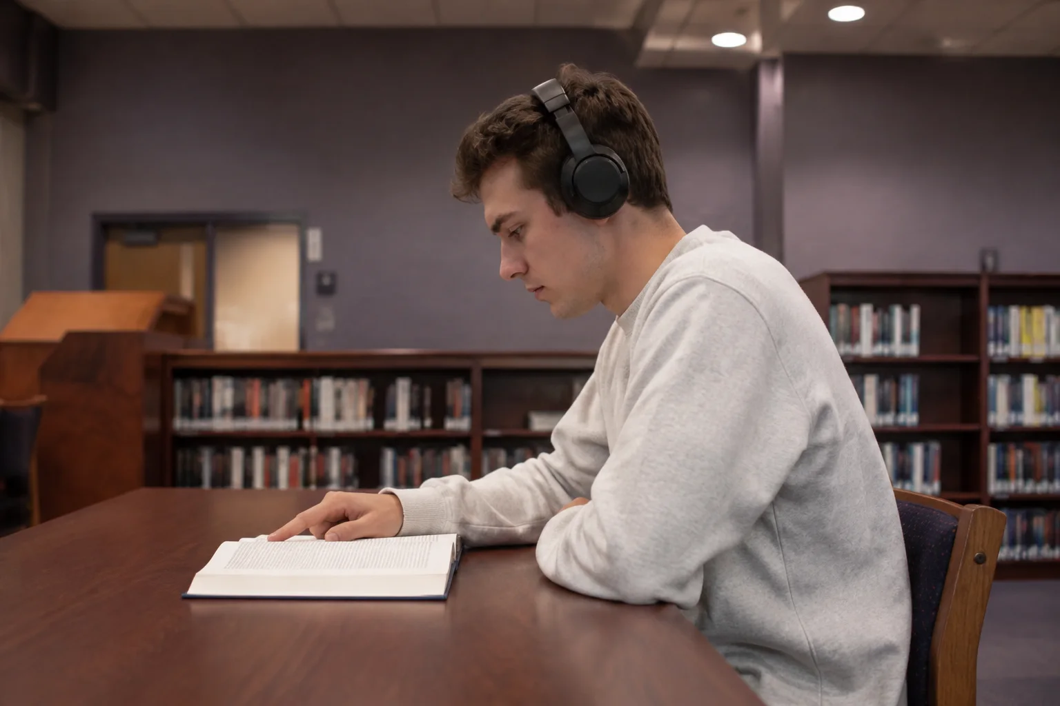 A learner listening through headphones with an open book in a library