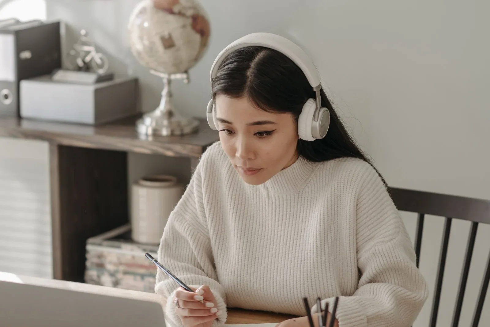 A learner wearing headphones takes notes beside a laptop