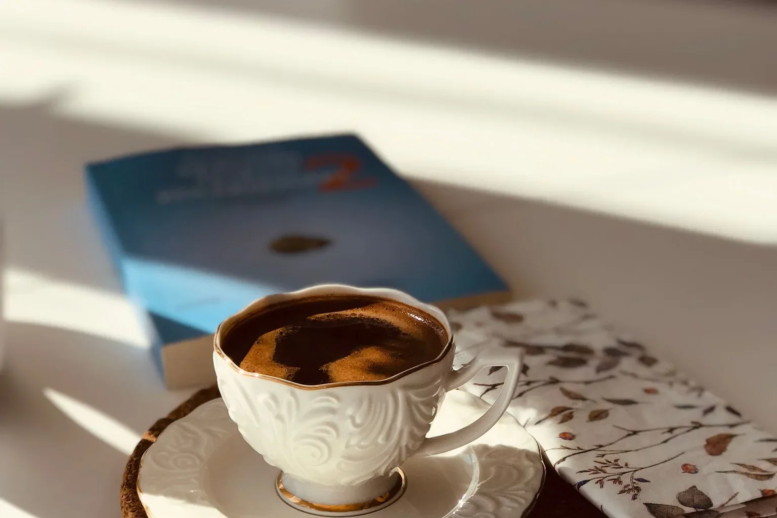 A small cup of espresso on a table beside a book
