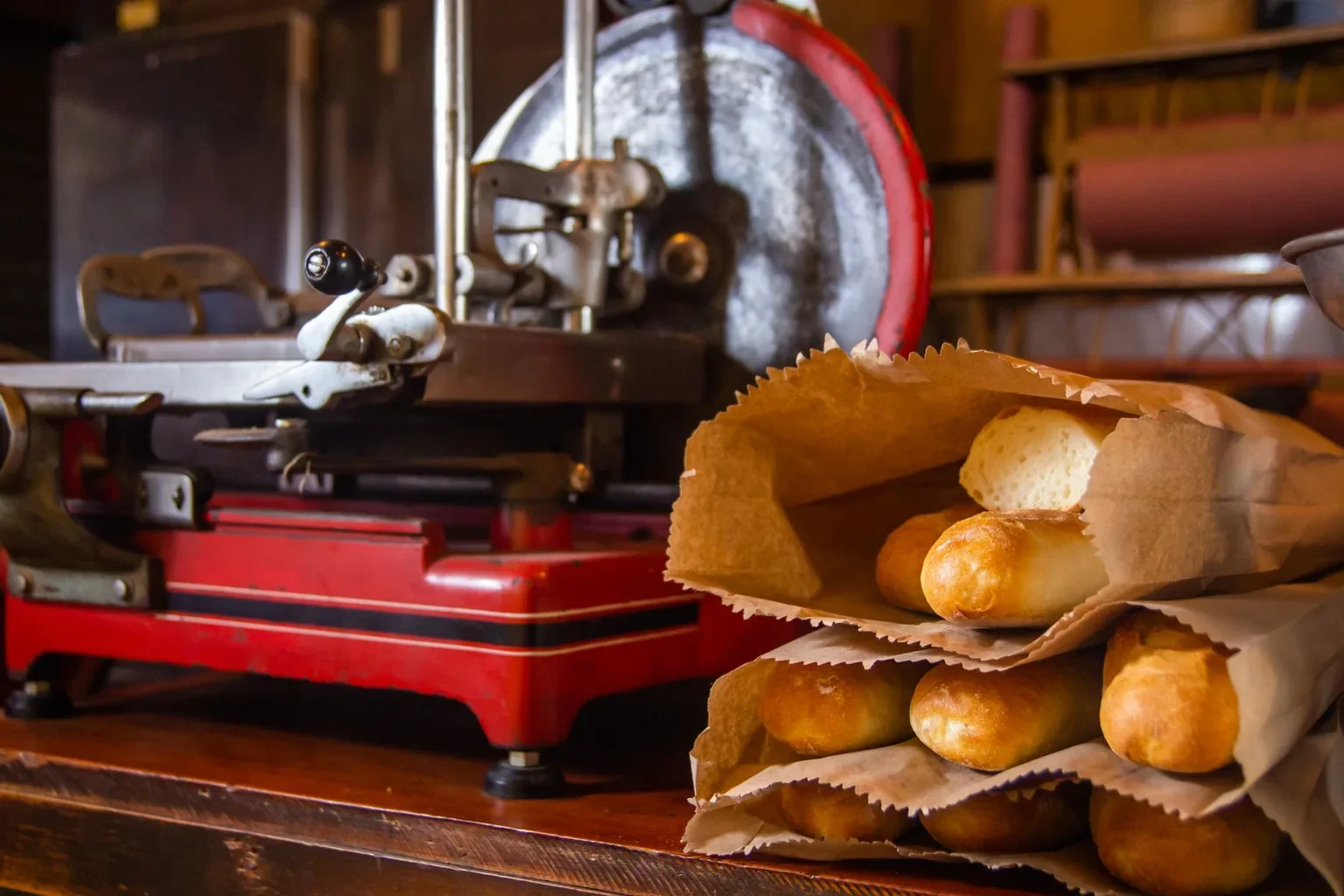 Baguettes in paper bags beside a bakery slicer