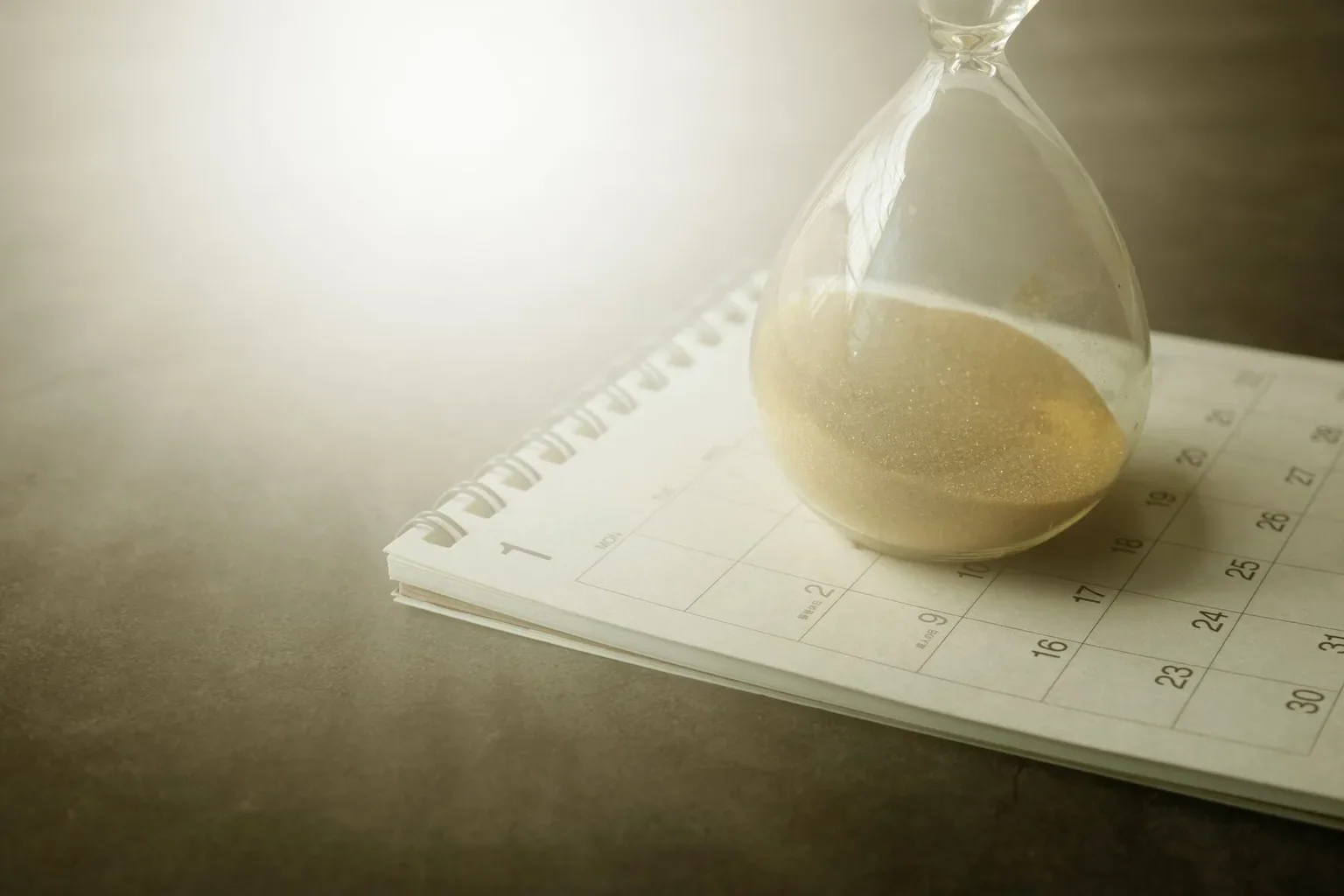 A glass hourglass resting on a paper calendar