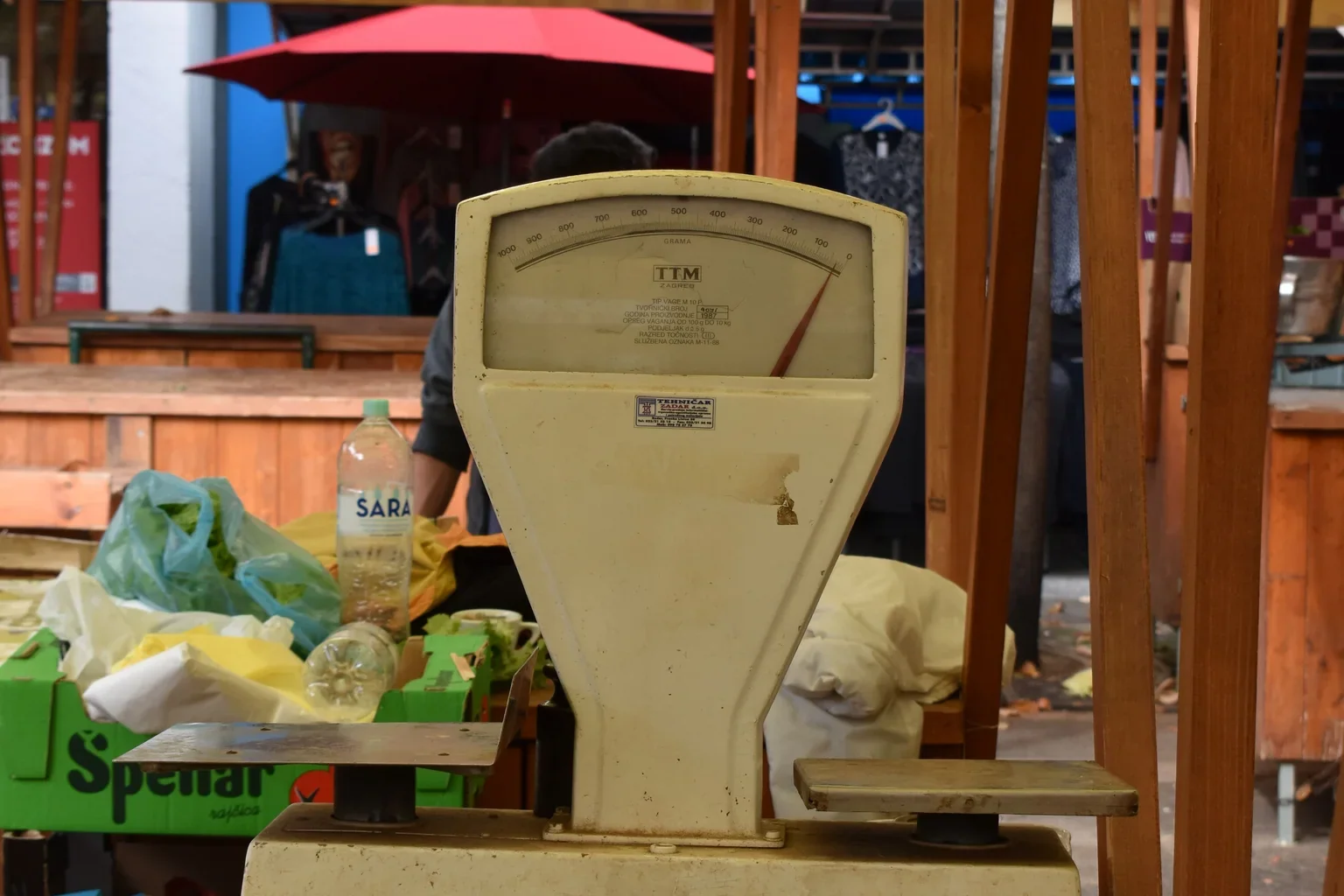 A market scale standing behind a display of cucumbers.