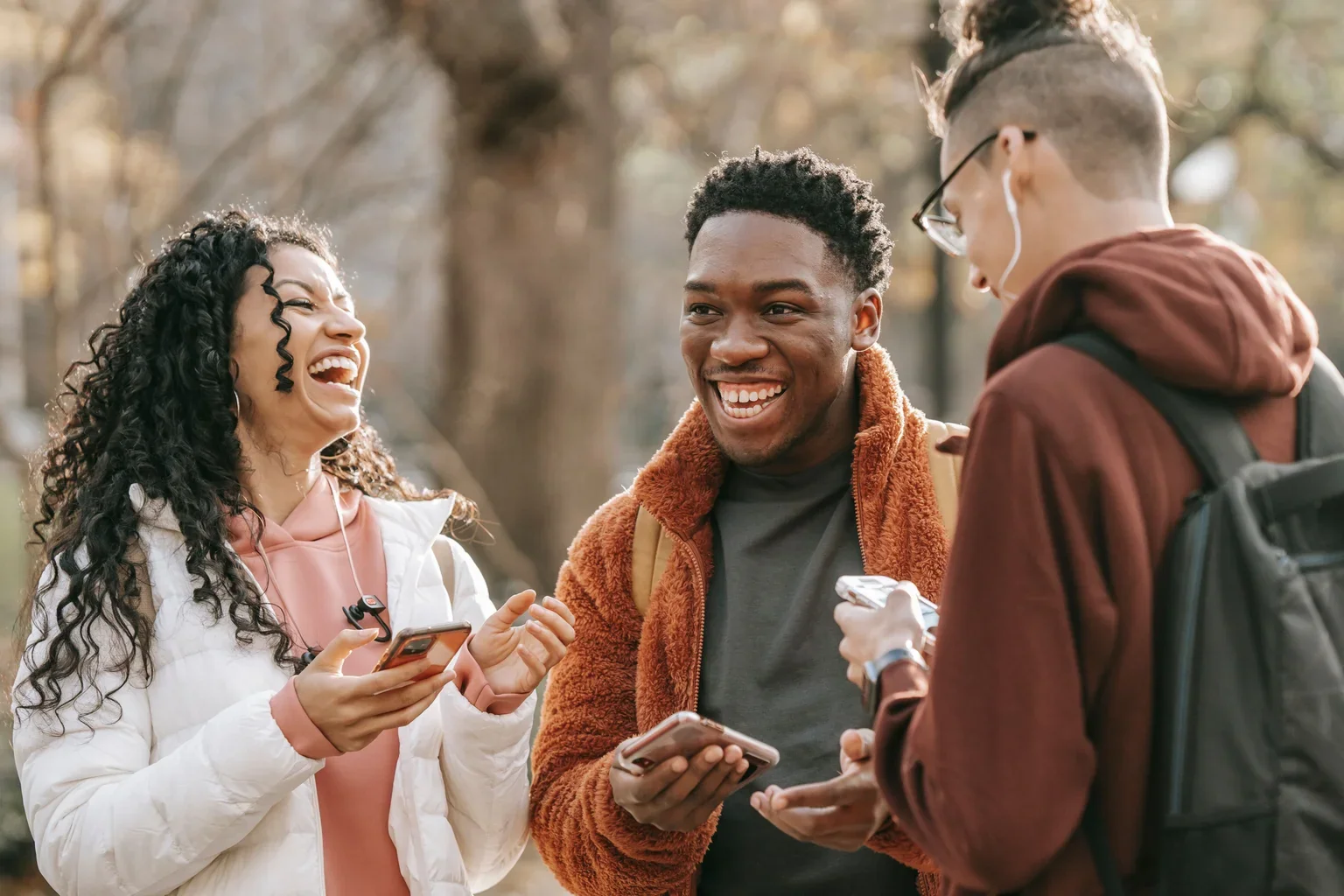 Friends talking outdoors while holding phones.