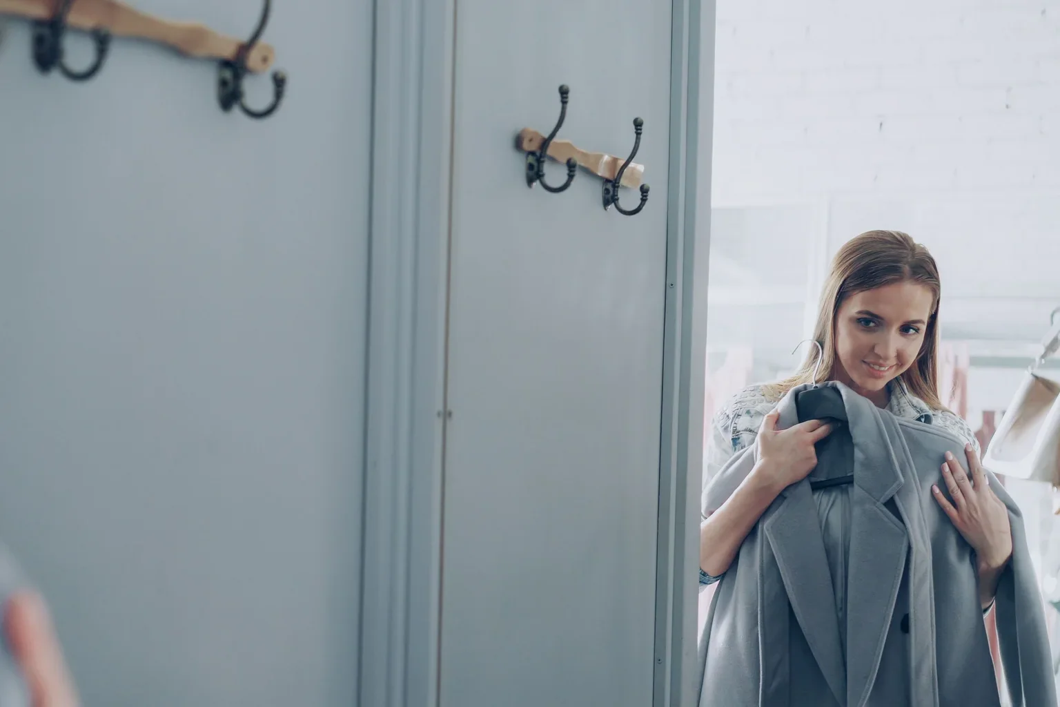 A shopper holding a jacket while looking in a fitting-room mirror.