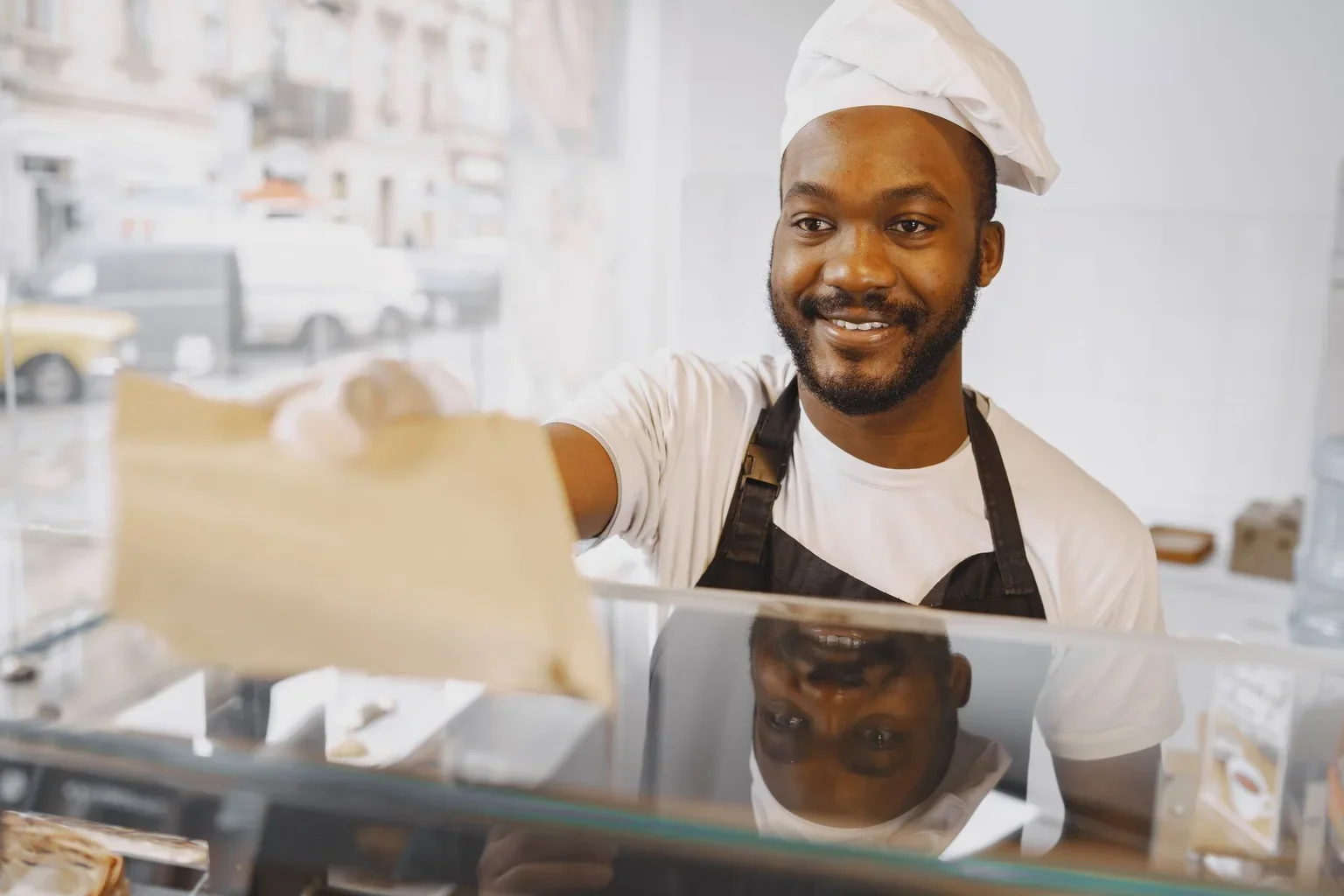 A baker holding a paper bag behind the counter