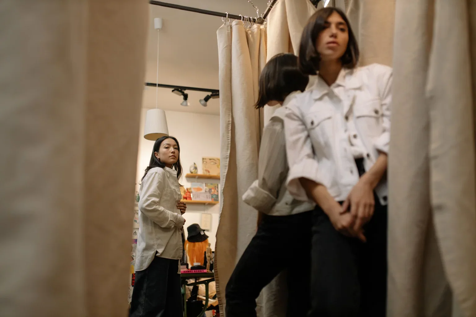 Shoppers beside mirrors and curtains in a clothing store.